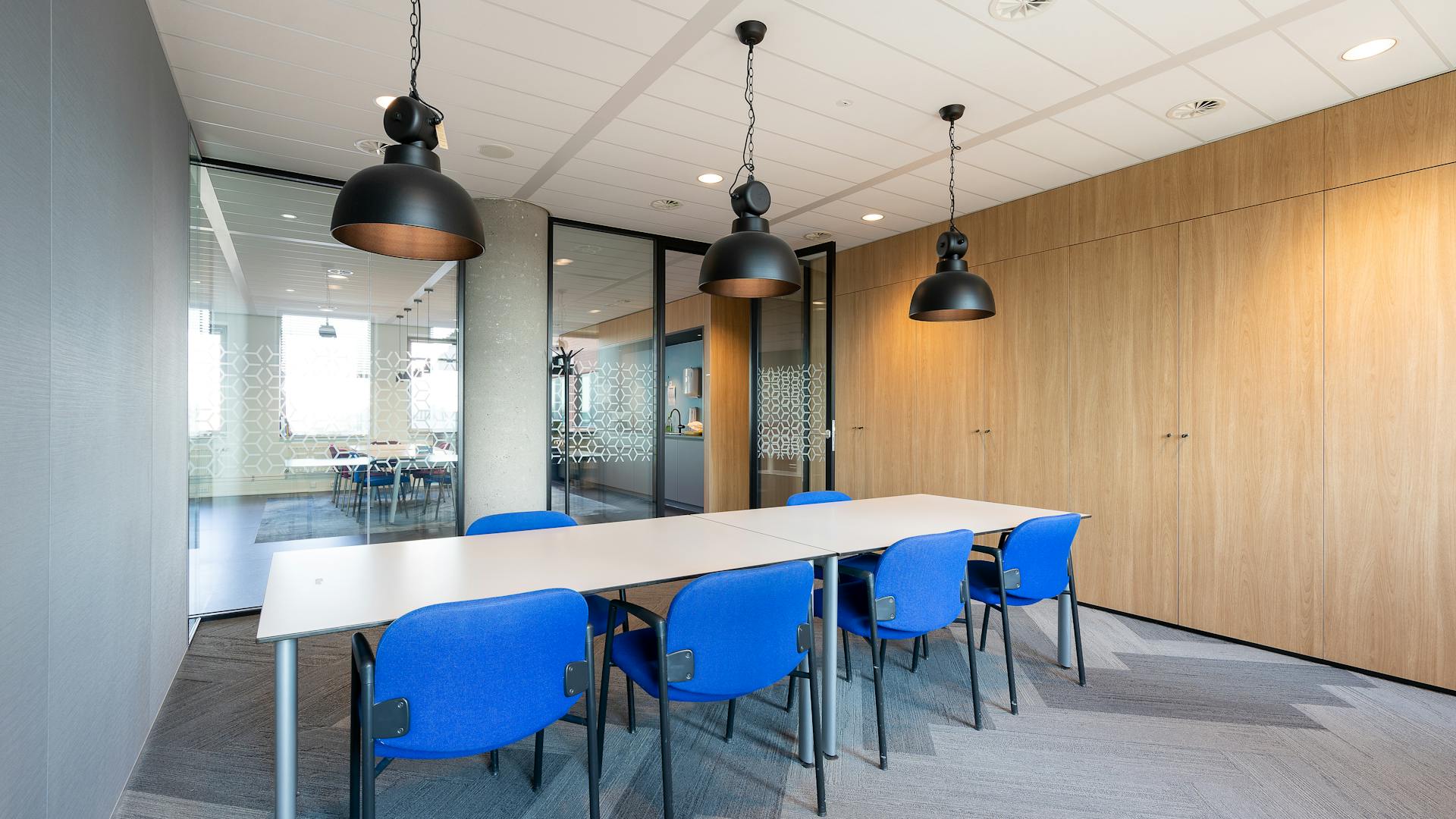 Spacious modern office meeting room with blue chairs and sleek pendant lights, ideal for professional settings.