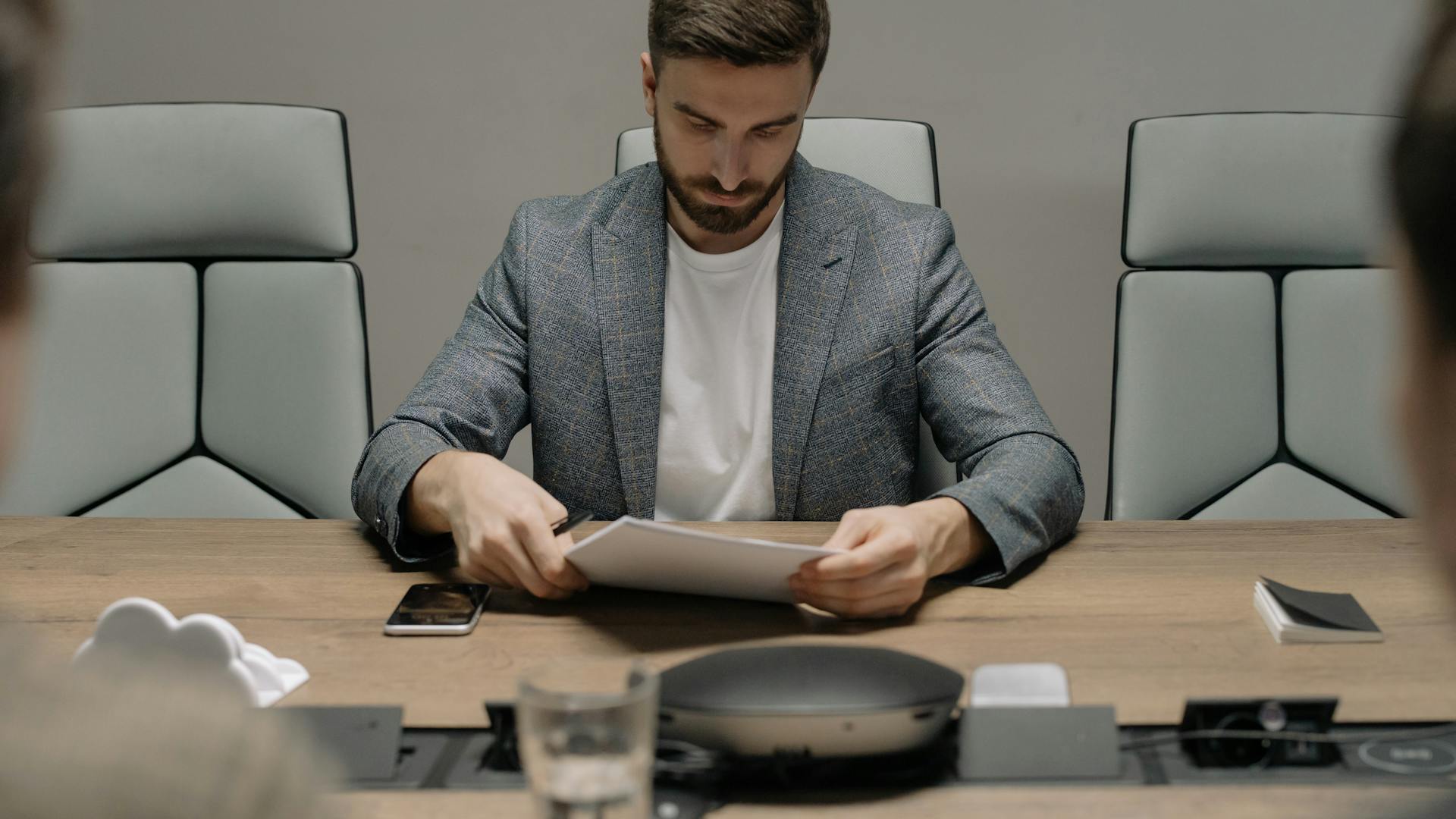 A focused businessman reads documents at a conference table, preparing for a meeting.