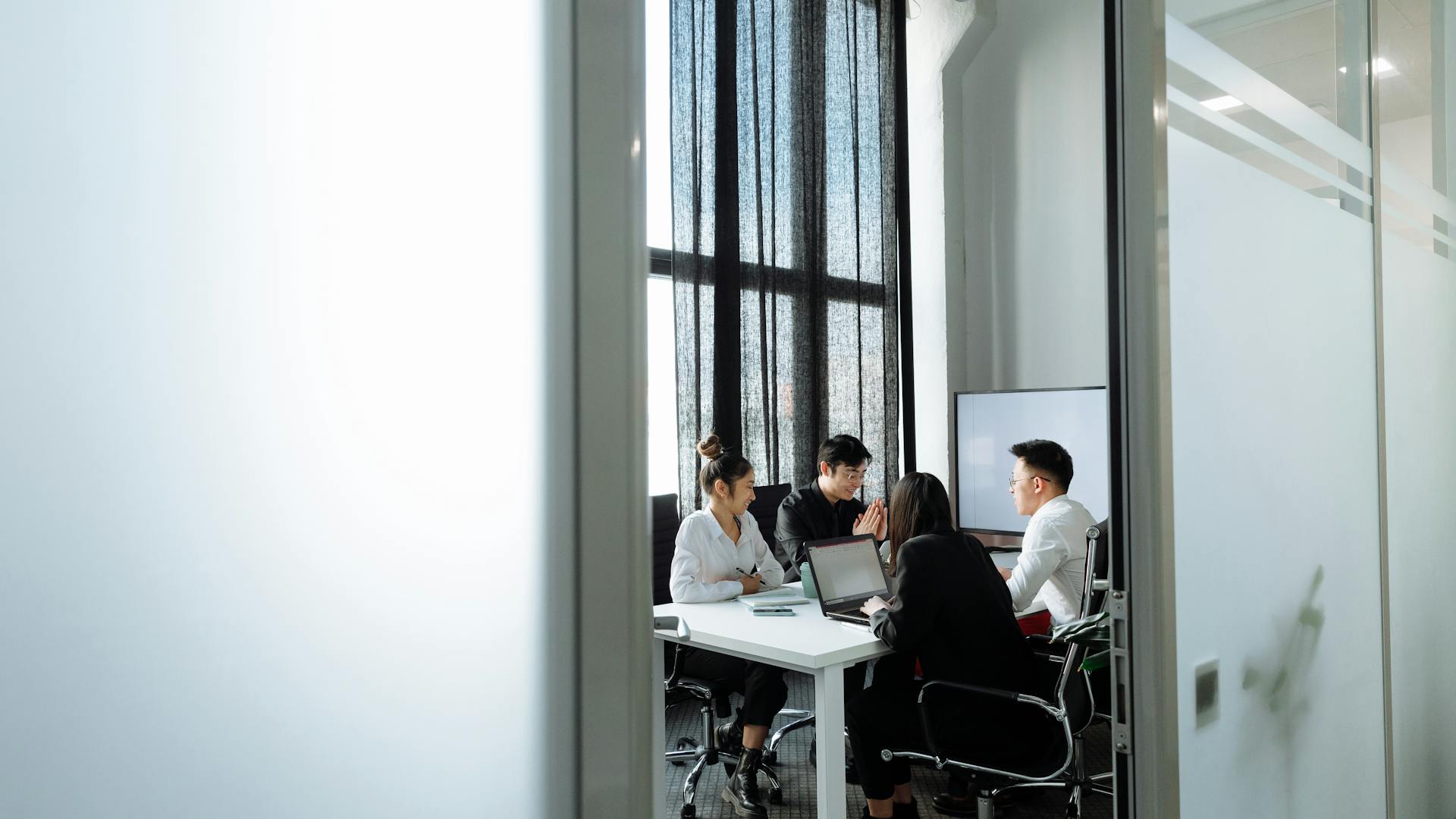 Group collaborating in a well-lit office room with large windows, discussing business strategies.