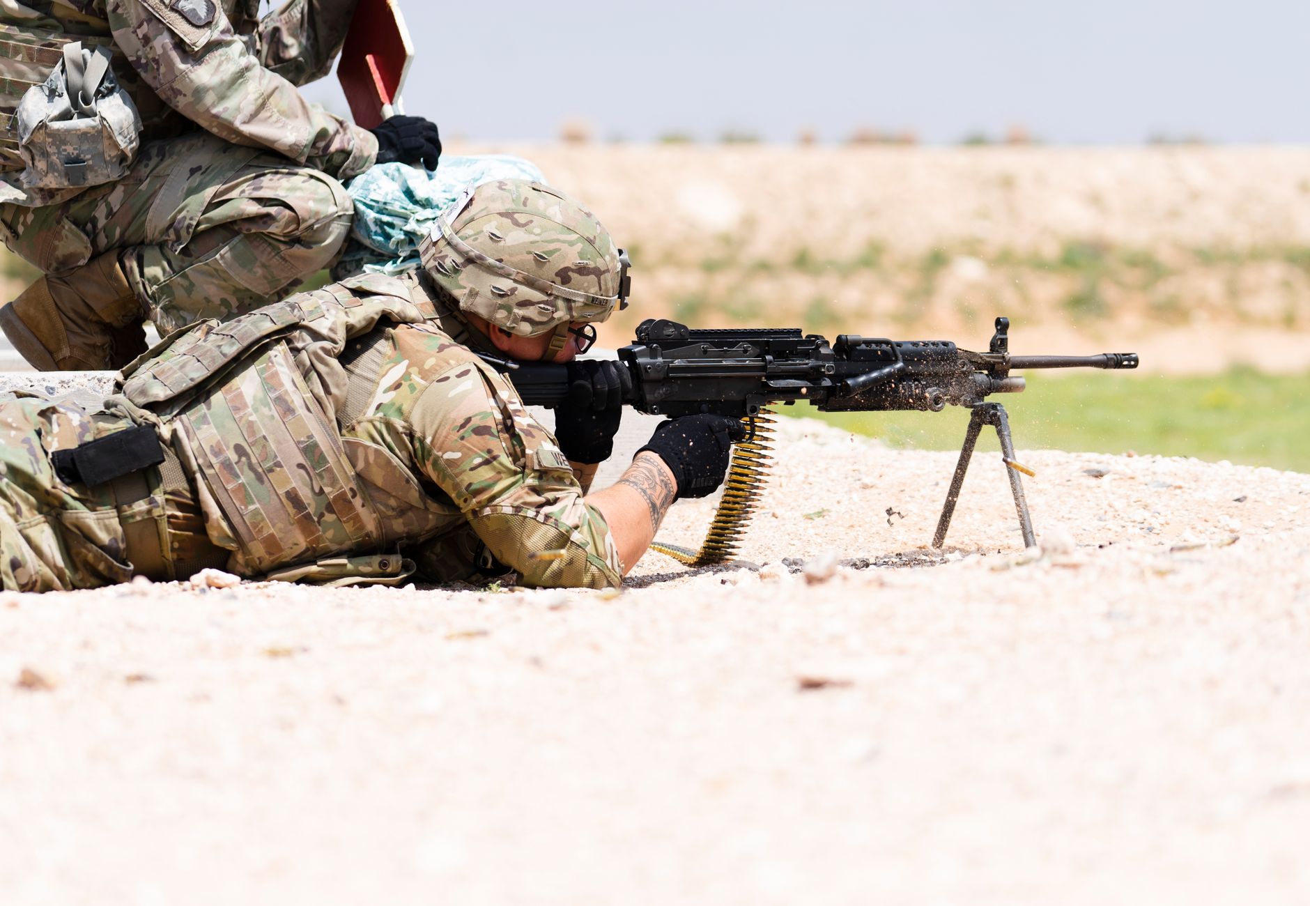 US soldier in camouflage uniform using a machine gun in outdoor military training.