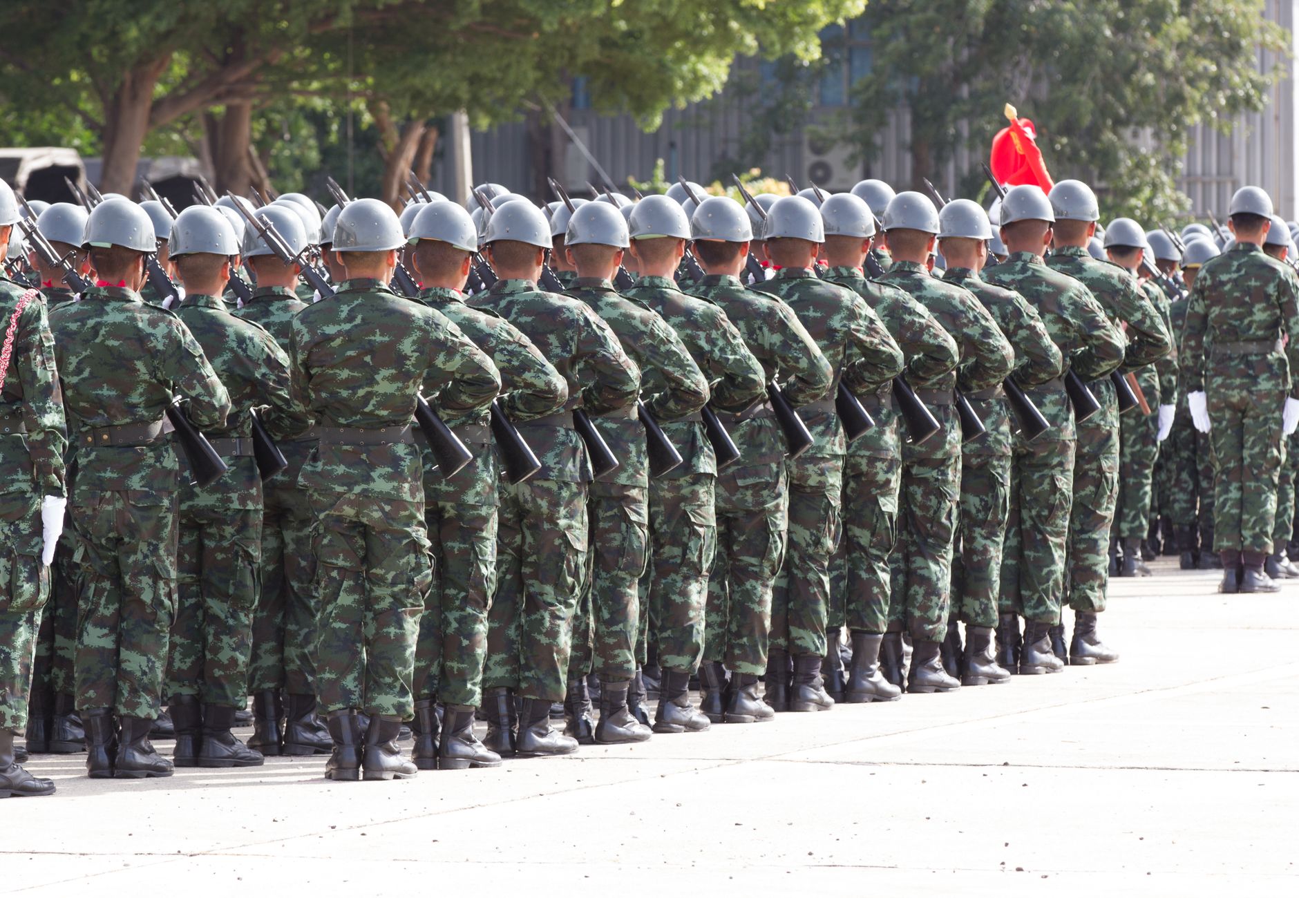 Back view unrecognizable soldiers with riffles wearing khaki uniform and hardhat lining up in rows during military ceremony