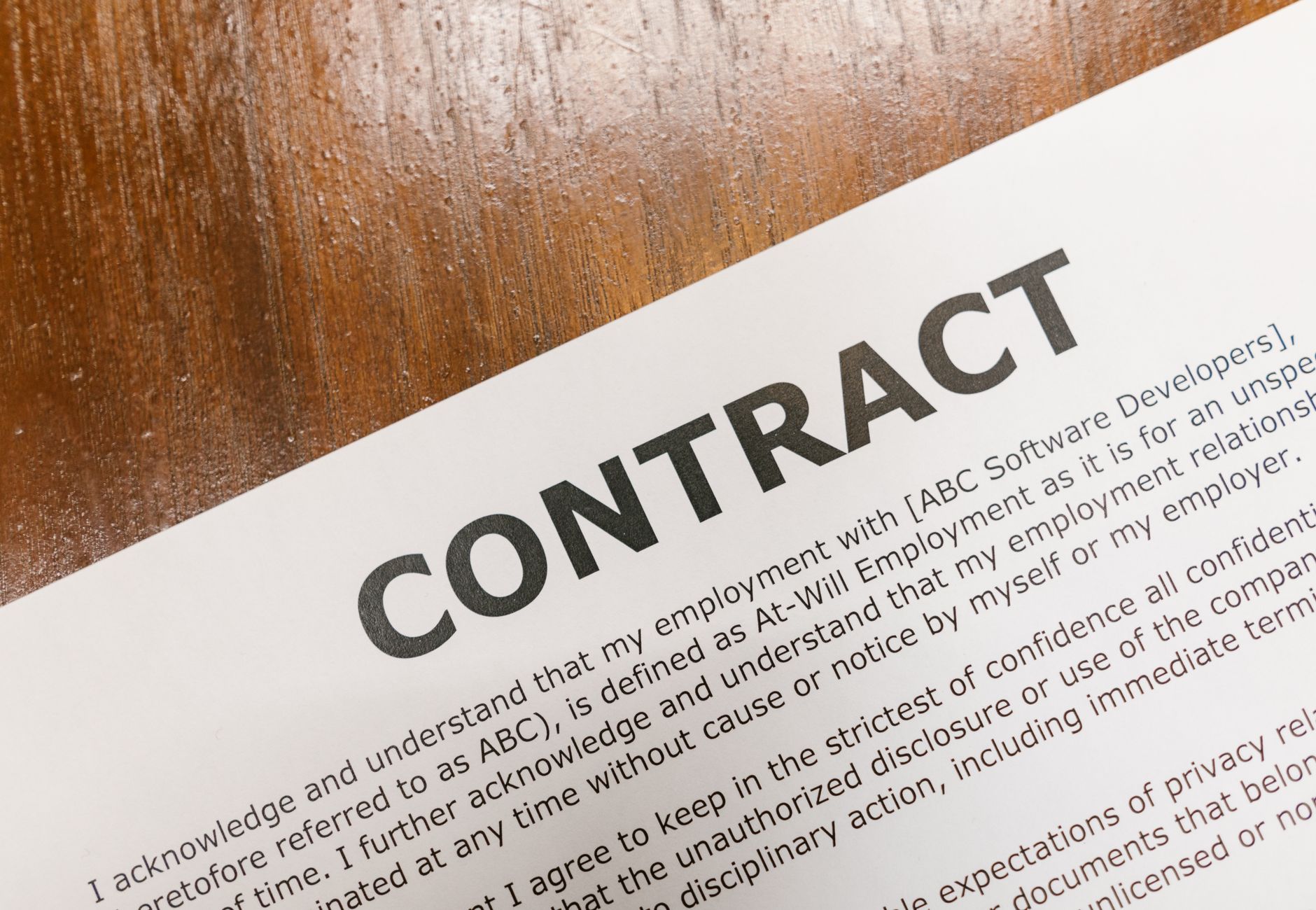 A detailed close-up of a printed contract document on a wooden table surface.