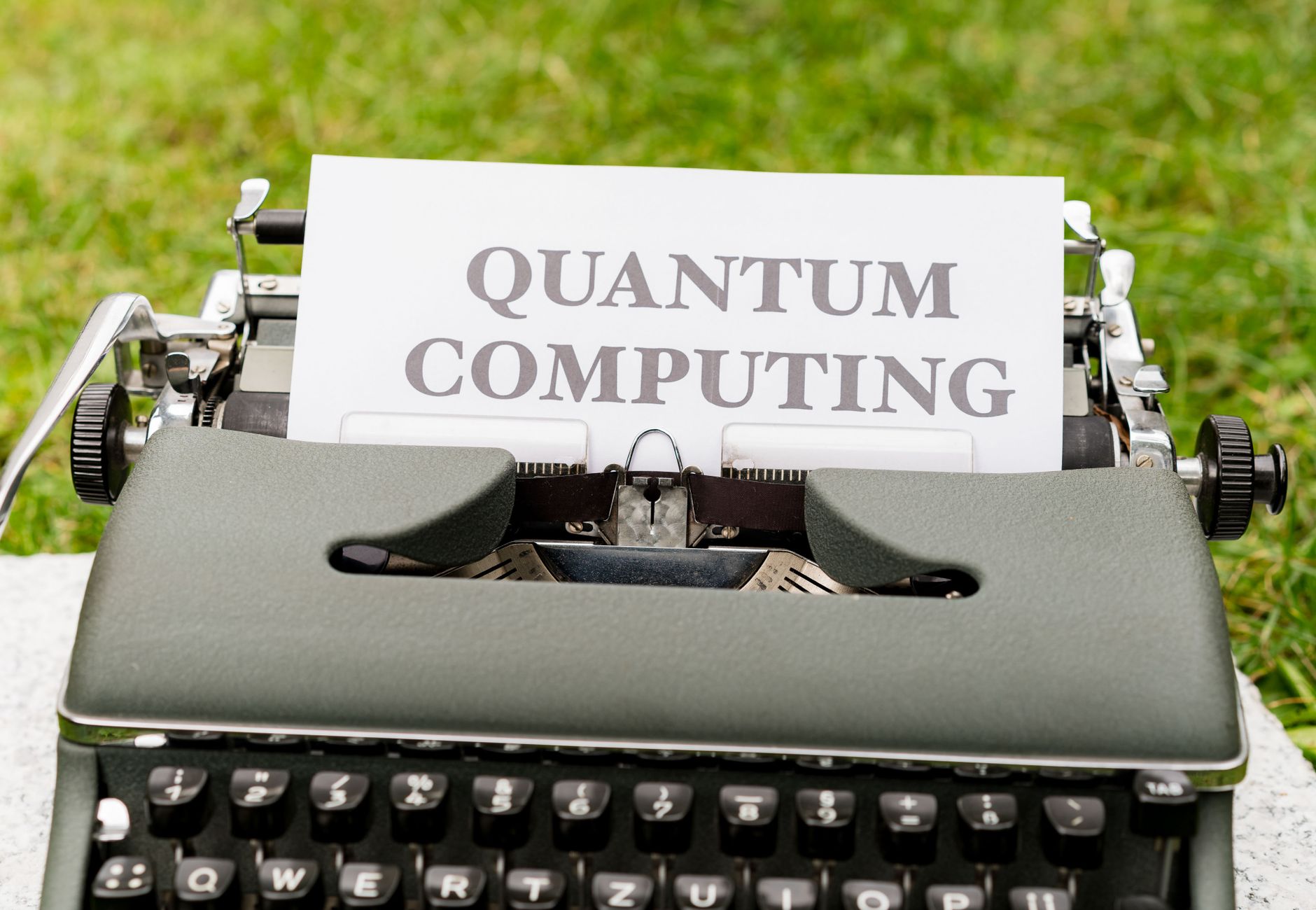 A typewriter with 'Quantum Computing' text outdoors on grass, blending old and new technologies.
