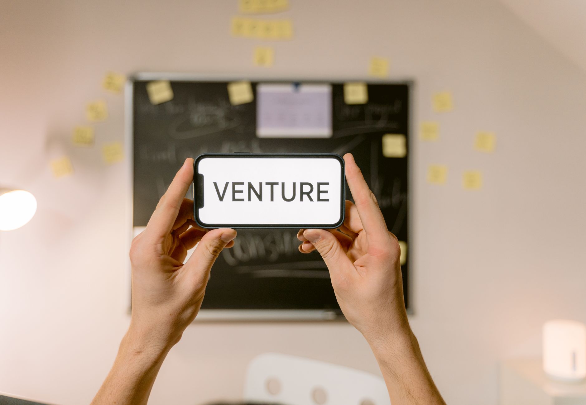 A smartphone displaying 'Venture' held by hands in an office setup. Ideal for business and startup themes.