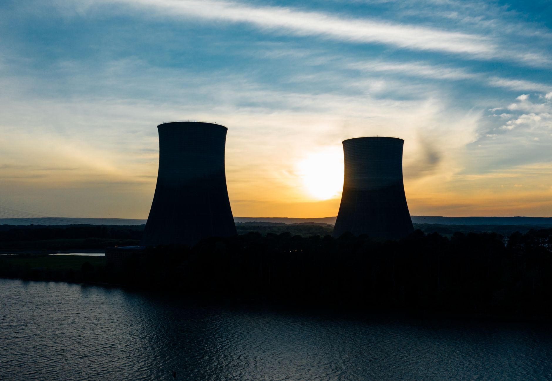 Identical cooling tower silhouettes on power plant near rippled river under colorful cloudy sky at sundown