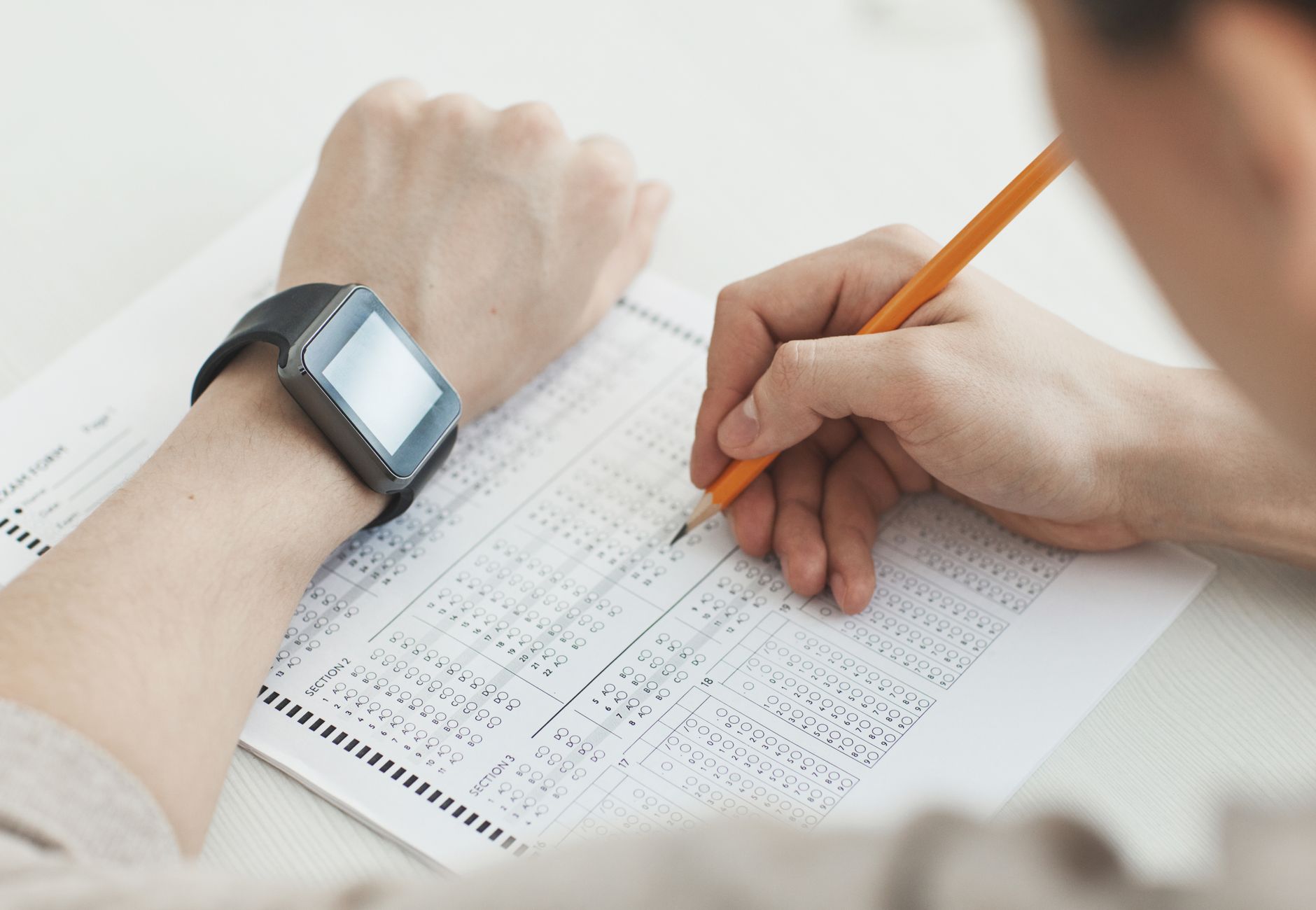 Close-up of a student writing answers on a test sheet with a pencil and smartwatch.